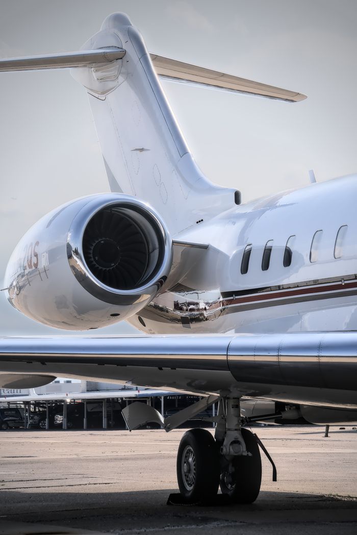 Close-up of a private jet engine and tail at airport tarmac in daylight.
